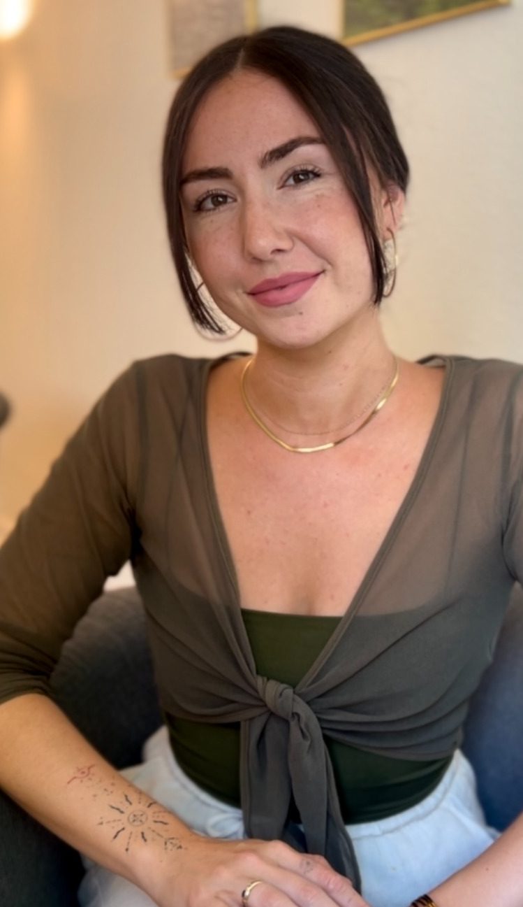 Das Bild zeigt Giorgia Nebuloni, eine Heilpraktikerin für Psychotherapie aus Köln, in einem grünen Garten sitzend. Sie trägt ein schwarzes Kleid und lächelt freundlich. Giorgia sitzt auf einer Holzbank, umgeben von verschiedenen Pflanzen und Blumen. Die entspannte und natürliche Umgebung strahlt Ruhe und Harmonie aus, was ihre therapeutische Philosophie widerspiegelt.
