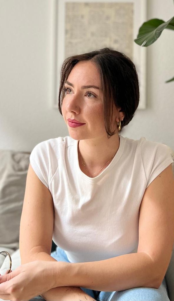 Giorgia Nebuloni Heilpraktikerin für Psychotherapie in Köln Das Bild zeigt Giorgia Nebuloni, eine Heilpraktikerin für Psychotherapie aus Köln, in einem grünen Garten sitzend. Sie trägt ein schwarzes Kleid und lächelt freundlich. Giorgia sitzt auf einer Holzbank, umgeben von verschiedenen Pflanzen und Blumen. Die entspannte und natürliche Umgebung strahlt Ruhe und Harmonie aus, was ihre therapeutische Philosophie widerspiegelt.